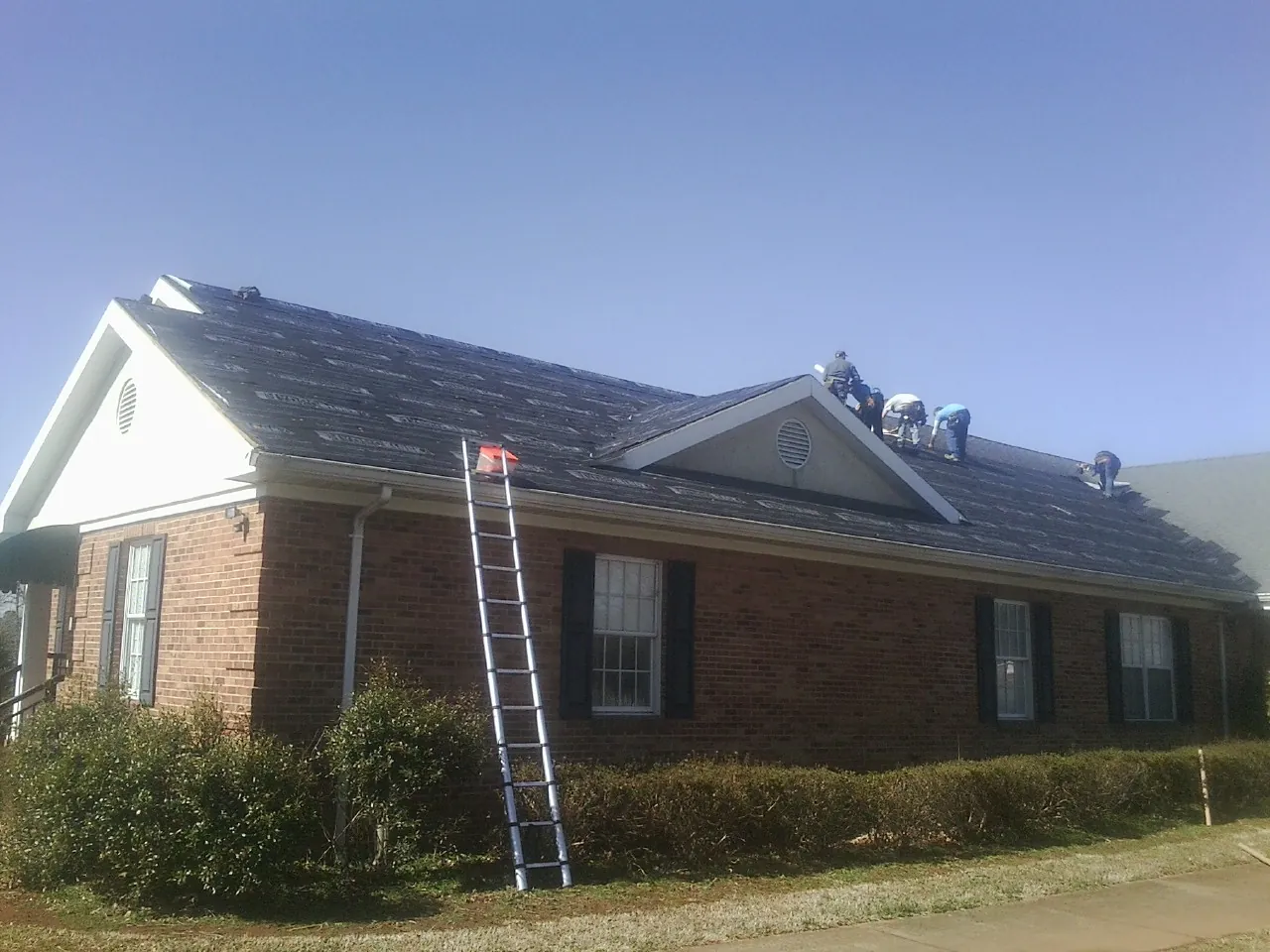 Crew tearing shingles off a brick ranch roof with a ladder set — Metal Roof Repair work by our crew in Mantua