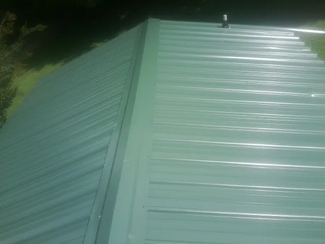 New green metal panels meeting at the ridge of a roof — Flat Roof Repair work by our crew in Mantua