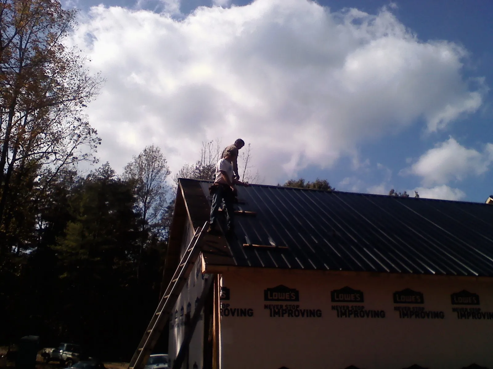 Roofer fastening dark metal panels high against a cloudy sky, from a Roof Inspection job in Mantua
